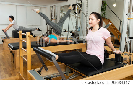 Young woman performing pilates on reformer in fitness studio 93684347
