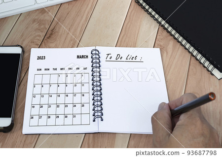 Hands with pen writing to do list with March 2023 calendar on notebook. Hands with pen writing to do list with March 2023 calendar on notebook. 93687798