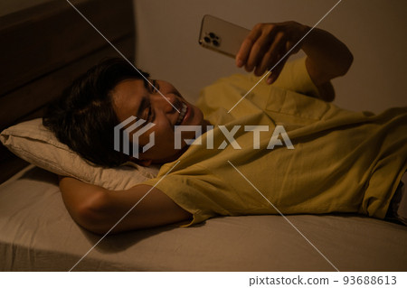 Sleep / Image of a man looking at a smartphone on the bed in the bedroom 93688613
