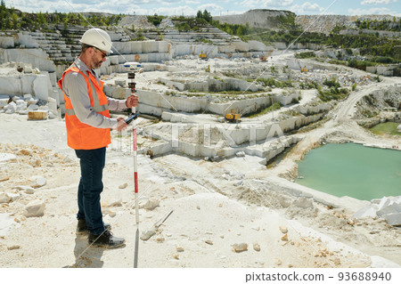 Male worker of marble quarry standing on its territory and adjusting theodolite 93688940