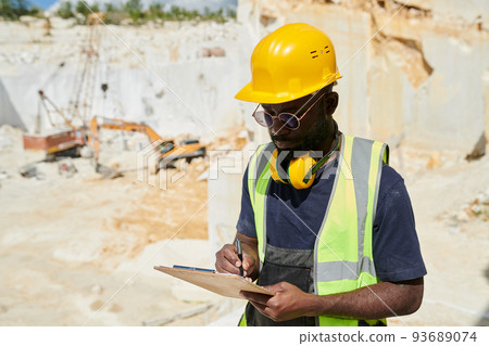 Young engineer in workwear making notes in working document in clipboard Young engineer in workwear making notes in working document in clipboard 93689074