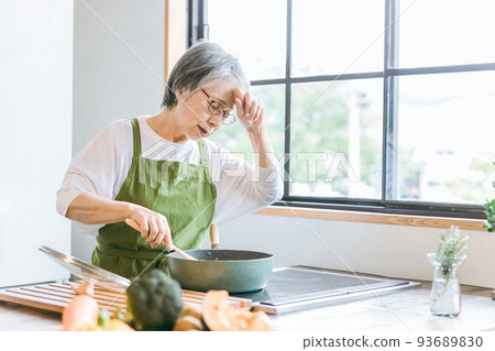 Senior woman using a frying pan in the kitchen (fatigue, poor physical condition) 93689830