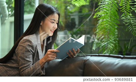 Elegant millennial business woman resting on couch in bright modern office and reading book Elegant millennial business woman resting on couch in bright modern office and reading book 93689881