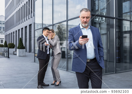 Two colleagues are gossiping at background behind the boss. workmate about bullying problem at work place in office in the break outside Male Coworkers employees man and woman Whispering Behind Back. Two colleagues are gossiping at background behind the boss. workmate about bullying problem at work place in office in the break outside Male Coworkers employees man and woman Whispering Behind Back. 93692103