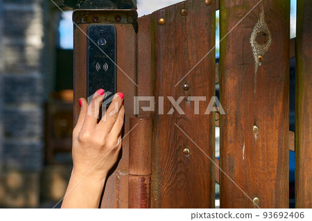 Woman's hand pressing a doorbell on a wooden fence in the garden 93692406
