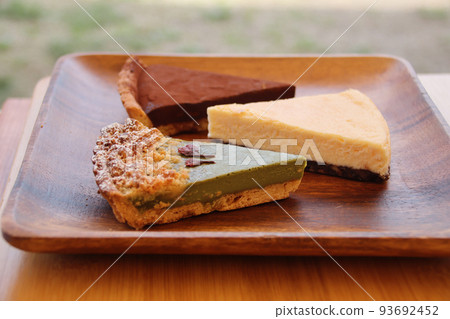 Matcha tart, cheesecake, chocolate tart and baked goods served on an acacia plate 93692452