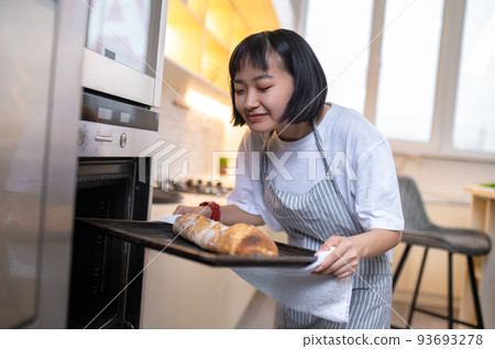 Young housewife baking something in the oven and looking busy Young housewife baking something in the oven and looking busy 93693278