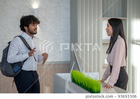 Indian young man with backpack talking to a girl on reception Indian young man with backpack talking to a girl on reception 93693306