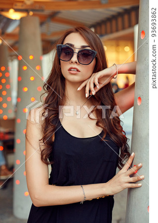 Close-up portrait of young elegant brunette in black dress and sunglasses, touching her face. Fashion street shot Close-up portrait of young elegant brunette in black dress and sunglasses, touching her face. Fashion street shot 93693862