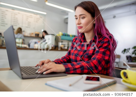 Young woman with pink hair with laptop computer sitting in cafe, intelligent female student working on net-book. 93694857