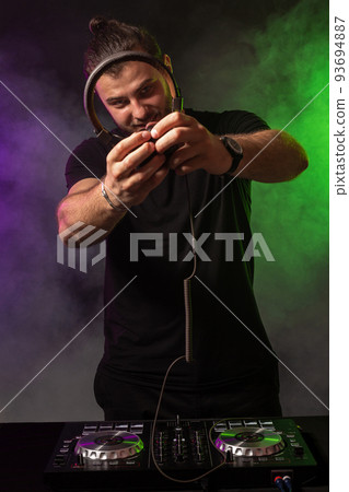 DJ playing music at mixer on colorful foggy background 93694887