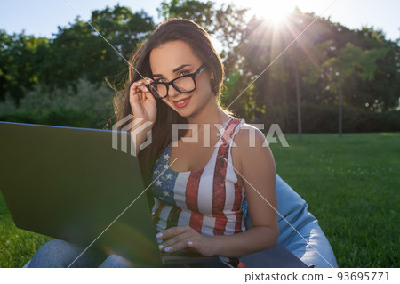 Pretty young woman sitting on bean bag use laptop while resting on grass in park on the sun 93695771