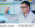 Serious clinician gazing at flask with blue liquid in laboratory 93696307