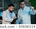 Young chemical technician checking liquid reagent in laboratory 93696314