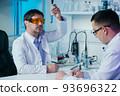 Male scientist in lab working in pharmaceutical studies and medical research with microscope and liquids in test tubes. 93696322