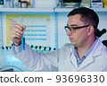 Serious clinician gazing at flask with blue liquid in laboratory 93696330