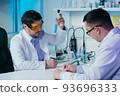 Male scientist in lab working in pharmaceutical studies and medical research with microscope and liquids in test tubes. 93696333