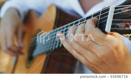 Close-up of the musician's playing hands. The guitarist plays the guitar. Professional guitarist plays guitar outdoors. Musician plays a classical guitar in the park. 93696716