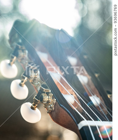 Close-up of the guitar head of a classical guitar with gold pegs. Part of a classical guitar on a blurry background in the park. Head of guitar with nylon strings. 93696769