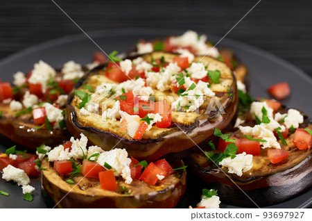 close up homemade eggplant salad with cheese and tomatoes, on a black table. close up homemade eggplant salad with cheese and tomatoes, on a black table. 93697927