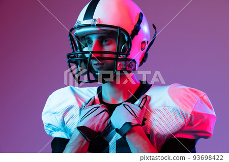 Close-up portrait of young man, american football player in helmet posing isolated over purple background neon light. 93698422