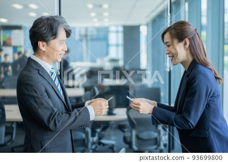 A veteran man and a young woman exchanging business cards in the office 93699800