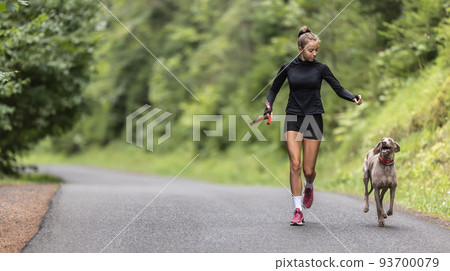Young female holding leash releases her dog on an empty road during jogging Young female holding leash releases her dog on an empty road during jogging 93700079
