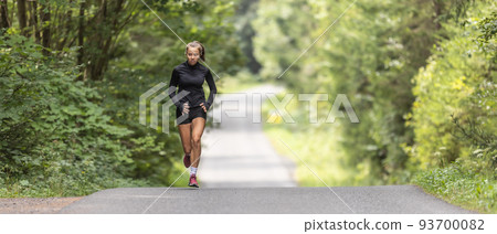 Young female athlete runs up the hill on an asphalt road in the nature 93700082