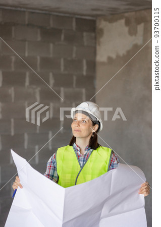 woman engineer in a white helmet and a protective vest holds a model house construction plan in her hands. construction sale and purchase woman engineer in a white helmet and a protective vest holds a model house construction plan in her hands. construction sale and purchase 93700115