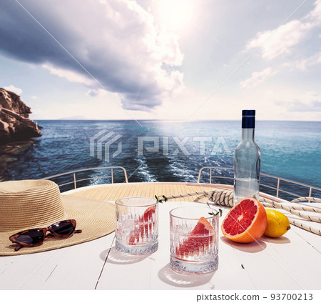 Bottle of pure water and two glasses and ripe grapefruit on deck of private yacht, cruise ship during summer vacation, outdoors. Vivid impressions, ad, fashion 93700213