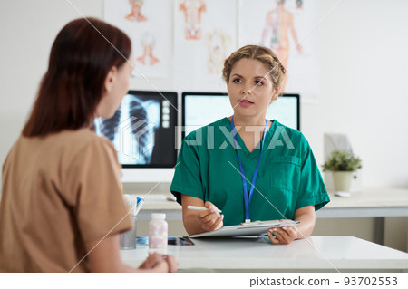 Young female doctor talking to female patient and writing down disease symptoms Young female doctor talking to female patient and writing down disease symptoms 93702553