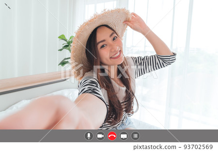 Young Asian woman blogger smiling in summer casual clothes and straw hat talking to facetime video calling with smartphone in bedroom. Using videochat online app with mic, video, phone, share screen, 93702569
