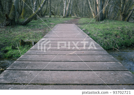 outdoor natural landscape with empty trail between trees through wooden bridge. Small wooden bridge in a forest in early spring 93702721