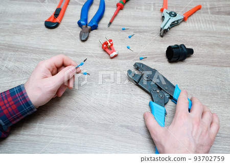 A male electrician changes the plug on an electric wire. Working with electrical tools. Stripper, crimp, screwdriver, wire cutters. Electrician connecting wires 93702759