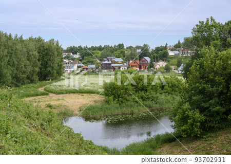 View of the pond, blooming meadow, forest and cottages in summer in Suzdal, Russia 93702931