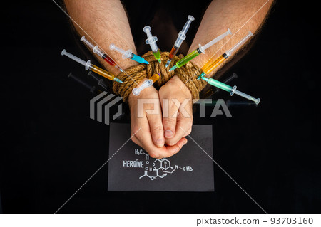 Many colorful syringes sticking from bound male hands. Isolated on black background. 93703160