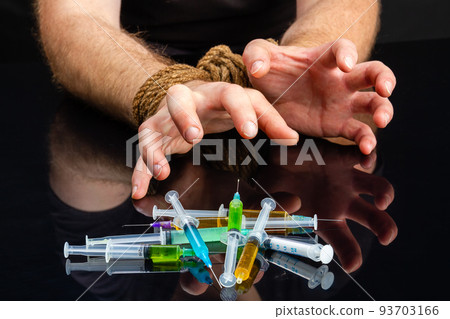 Close-up bound male hands craving for syringes filled with drugs. Drug addiction dependence and hostage concept. Close-up bound male hands craving for syringes filled with drugs. Drug addiction dependence and hostage concept. 93703166