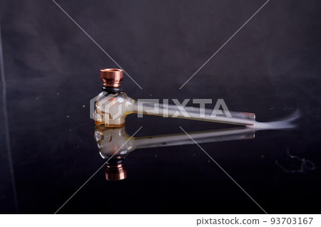 Glass pipe for crack or crystal meth on reflective mirror surface. Smoke on black background. Glass pipe for crack or crystal meth on reflective mirror surface. Smoke on black background. 93703167