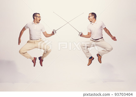 Portrait of two men in a suit fighting with swords in a jump isolated over grey studio background Portrait of two men in a suit fighting with swords in a jump isolated over grey studio background 93703404