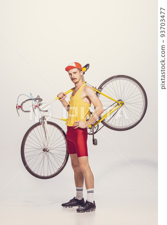 Portrait of young man in colorful clothes, uniform holidng bike on shoulder, posing isolated over grey background Portrait of young man in colorful clothes, uniform holidng bike on shoulder, posing isolated over grey background 93703477