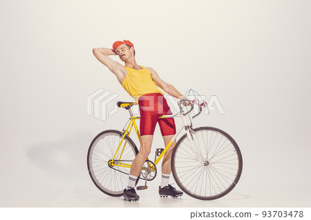 Portrait of young man in colorful clothes, uniform riding bike isolated over grey background. Looking relaxed. Chilling Portrait of young man in colorful clothes, uniform riding bike isolated over grey background. Looking relaxed. Chilling 93703478