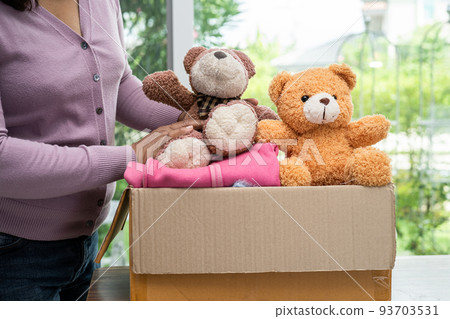 Holding clothing donation box with used clothes and doll at home to support help for poor people in the world. 93703531