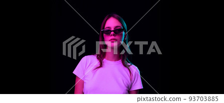 Portrait of pretty young girl, student wearing white tee isolated on dark background in pink neon light. Concept of beauty, art, fashion, emotions Portrait of pretty young girl, student wearing white tee isolated on dark background in pink neon light. Concept of beauty, art, fashion, emotions 93703885