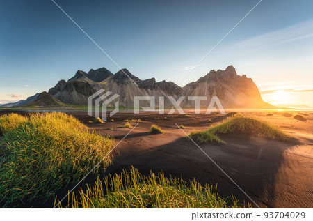 Sunrise over Vestrahorn mountain and clump of grass on black sand beach in Stokksnes on the southeastern at Iceland Sunrise over Vestrahorn mountain and clump of grass on black sand beach in Stokksnes on the southeastern at Iceland 93704029
