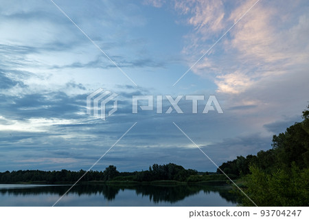 a beautiful blue lake with green tree in the foreground under a dramatic blue dusk sky 93704247
