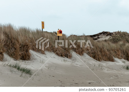 An orange lifebuoy and a sign on the shore under a cloudy sky. Dry grass. Seaside landscape. 93705261