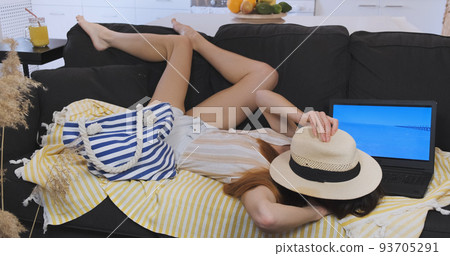 Young woman dreaming about sea vacation, couch lying in apartment. Holiday waiting at home, humor concept. Boring summer vacations indoors. Sad woman imitates travel, expecting weekend 93705291