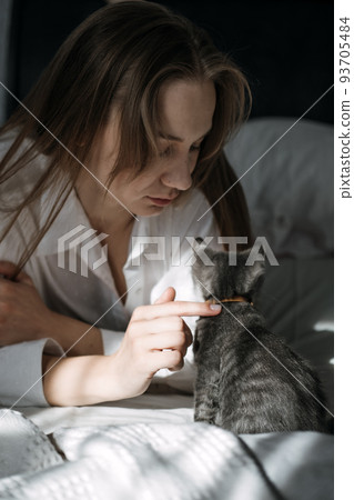 Candid portrait of young woman is resting with kitten pet on the bed at home one sunny day. Candid portrait of young woman is resting with kitten pet on the bed at home one sunny day. 93705484