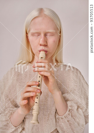 Portrait of young albino woman with white hair enjoying playing on flute on white background 93705513
