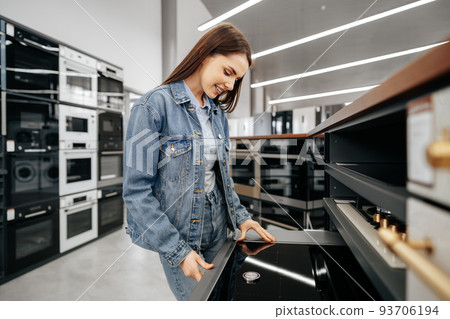 Young brunette woman choosing new electric stove in a hypermarket 93706194